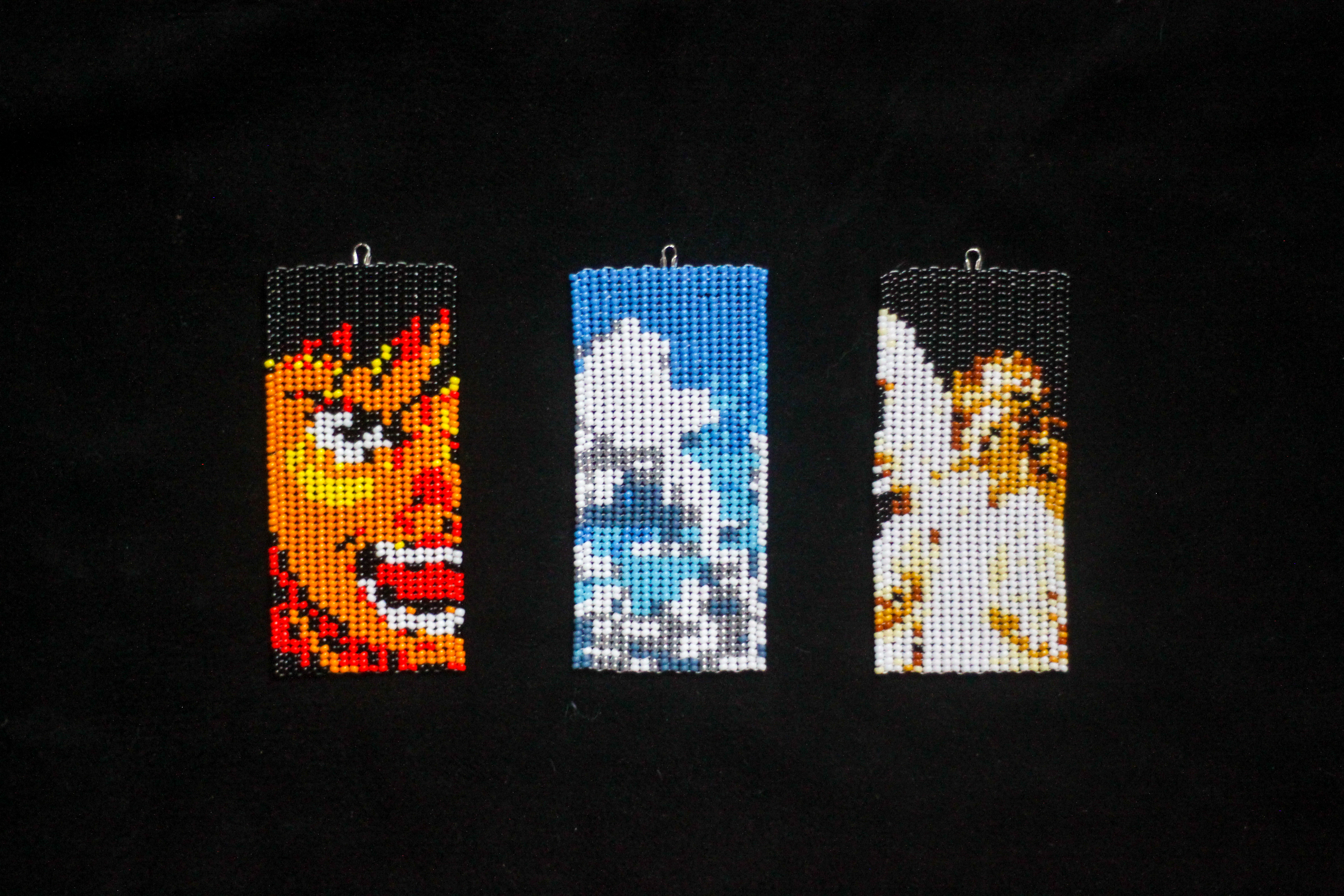 A close-up shot of three rectangular beaded tokens on black hide. The left-most depicts a face; the centre-most depicts a cloudy sky; the right-most depicts an angel.